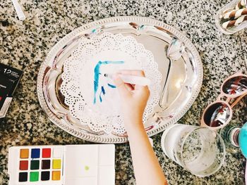 Cropped hand holding paintbrush by various objects on table