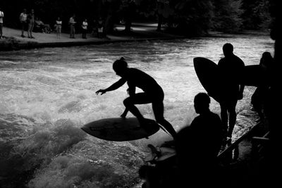 Silhouette people surfboarding on river