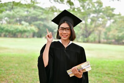 Student wearing graduation gown while standing on field at park