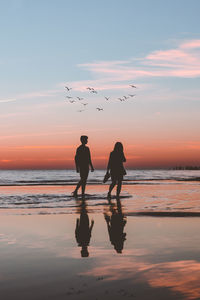 Silhouette people on beach against sky during sunset