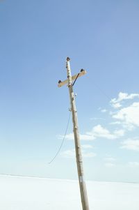 Electric pole on snow covered field against sky