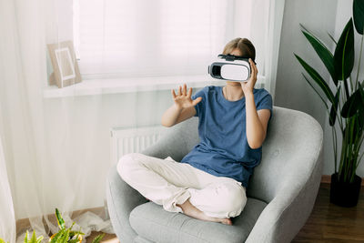 The girl is sitting in a chair with virtual glasses studying online or playing virtual games.