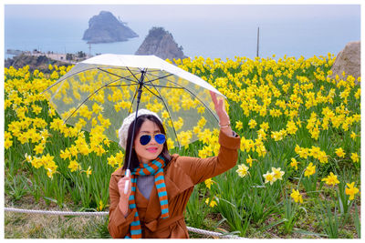 Smiling woman holding umbrella against yellow flowering plants
