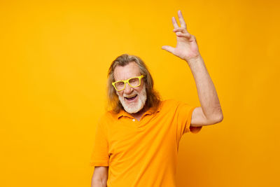 Senior man gesturing against yellow background