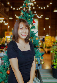 Portrait of young woman standing against christmas tree