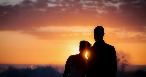 Silhouette couple standing at beach against sky during sunset