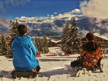 Rear view of women sitting on snowcapped mountain against sky