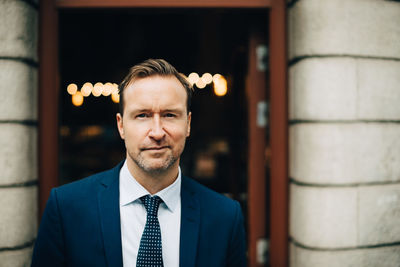 Portrait of confident mature businessman standing against building in city