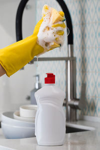 White bottle with dishwashing gel against the background of a sink and pouring foam from a sponge.