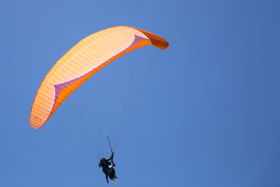 Low angle view of man paragliding against clear blue sky