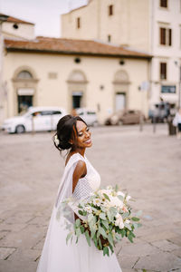 Side view of bride standing with flowering plant in city