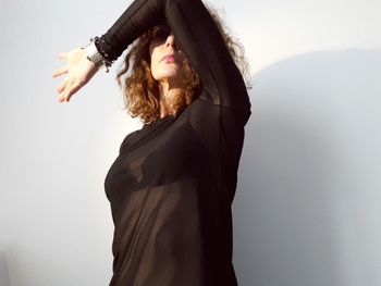 Mature woman wearing black top while standing against white wall