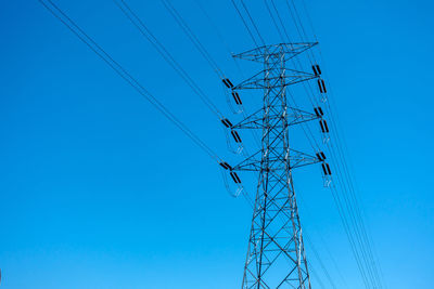 Low angle view of electricity pylon against clear blue sky