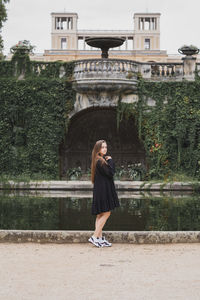 Woman standing by fountain against trees