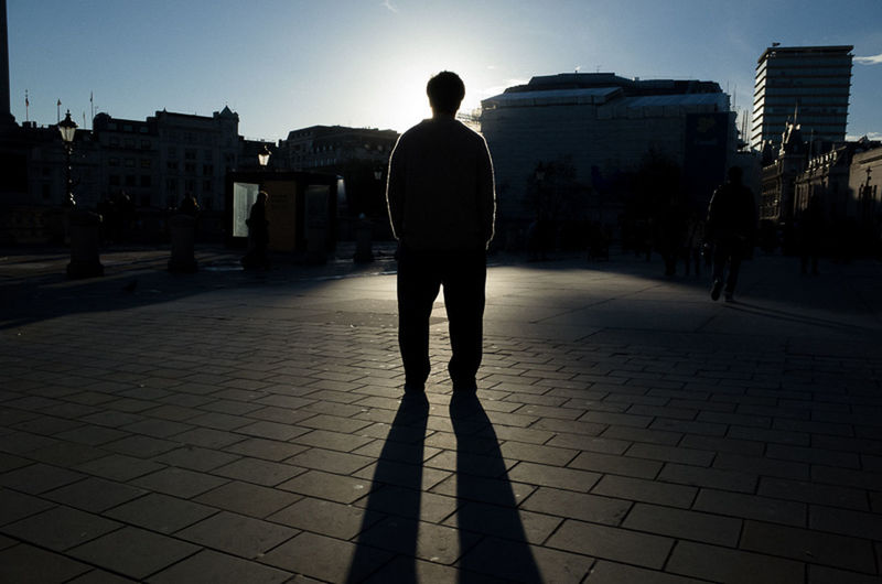 building exterior, full length, architecture, rear view, walking, built structure, lifestyles, city, silhouette, street, men, city life, standing, shadow, leisure activity, sidewalk, person, sunlight