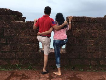 Rear view of friends standing by retaining wall against sky