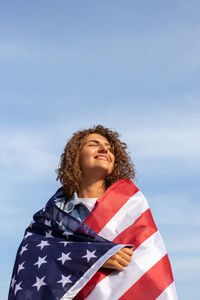 Portrait of young woman looking away against sky with american flag