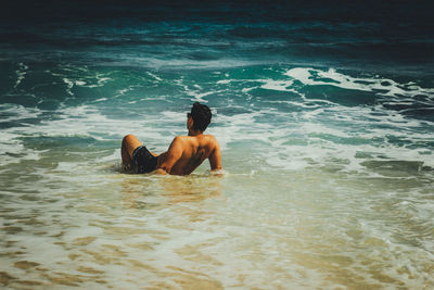 Rear view of shirtless man lying in sea
