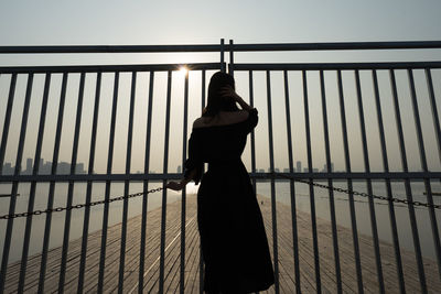 Rear view of woman standing by gate at pier