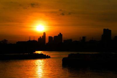 Silhouette buildings by river against romantic sky at sunset