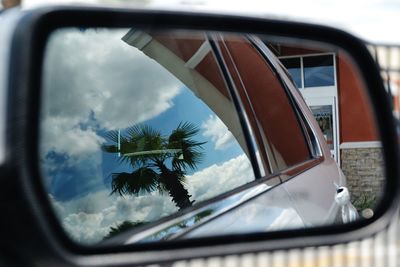 Reflection of car on side-view mirror against sky