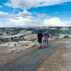 Rear view of boys walking on road by mountains against sky