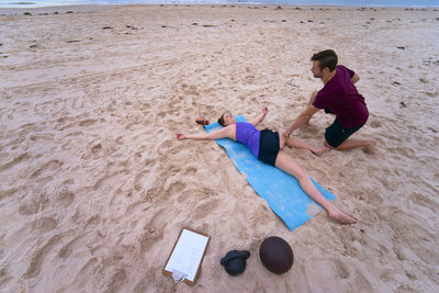 Fitness instructor assisting woman in exercising at beach