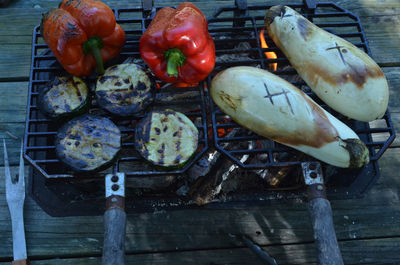 Hibachi grill with flame on white eggplant halves, red bell pepper, zucchini slices, red hot coals