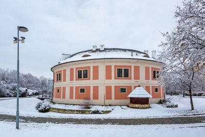 Snow covered field by building against sky