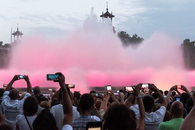 People photographing illuminated fountain spraying water in city