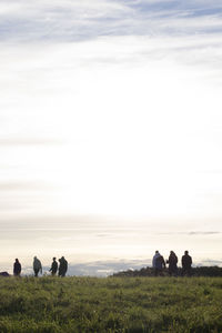 Rear view of people sitting on field against sky