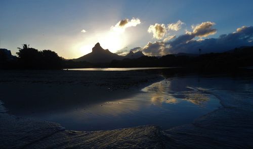 Scenic view of lake by silhouette mountain against sky during sunset