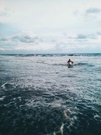 Man with surfboard walking in sea against cloudy sky