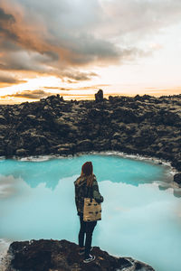 Rear view of woman standing on rock by sea against sky
