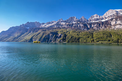 Scenic view of lake by rocky mountains against clear blue sky