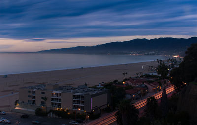 Illuminated cityscape by sea against sky at sunset