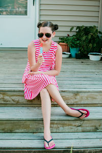 Full length of girl wearing sunglasses sitting outdoors with popsicle 