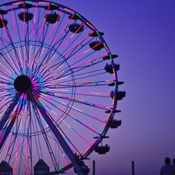 Low angle view of illuminated ferris wheel against clear sky at dusk