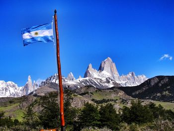 Flag on snowcapped mountains against blue sky
