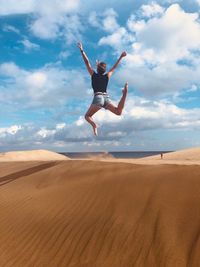 Rear view of woman jumping over sand in desert against sky