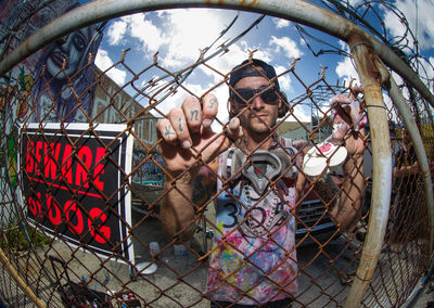 Portrait of man standing by fence against sky