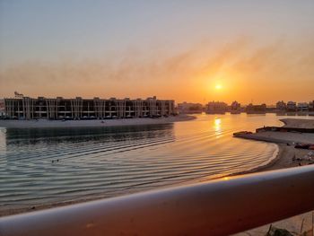 Sea by buildings against sky during sunset