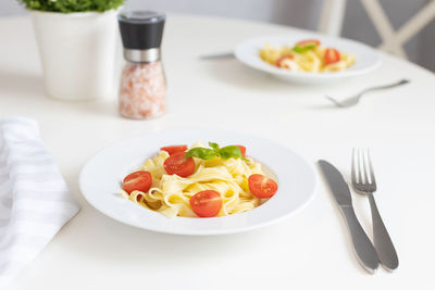 Italian pasta, pasta with cherry tomatoes and a sprig of basil in a white plate on a white table. 