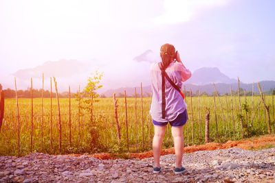 Rear view of woman standing on field against sky