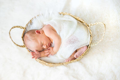High angle view of baby sleeping in basket on bed