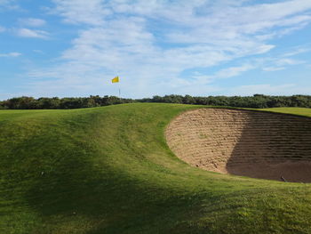 Sand trap at golf course against cloudy sky