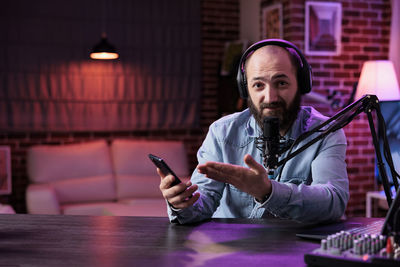 Man with headphones holding smart phone by mic in recording studio