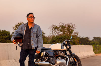 Summer travel on a motorcycle, motorcycle driver in black leather jacket stands on road with vintage 