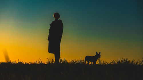 Woman with dog standing on field against sky during sunset