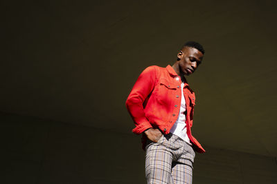 Stylish young man in red jacket and checked pants outdoors